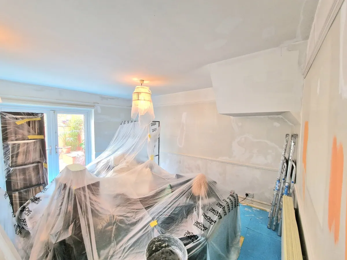 A living room mid-preparation with furniture under plastic sheeting