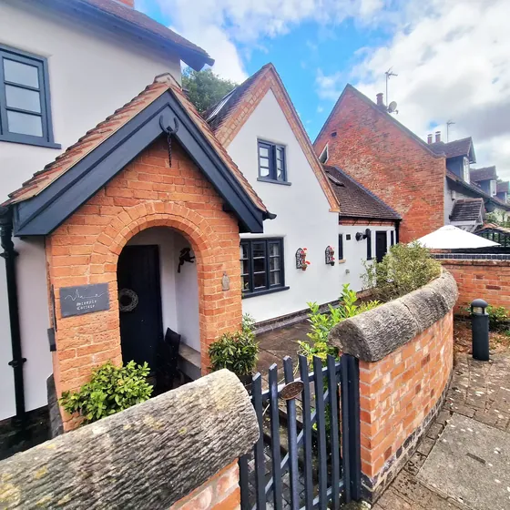 White rendered cottage with dark grey windows and a red brick porch, seen from the street