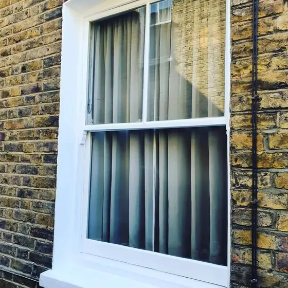 White sash window and stone surround in a brick wall