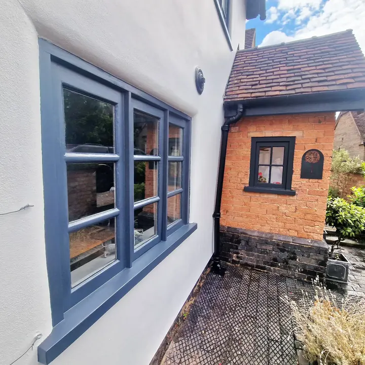Finished dark grey windows on a white rendered cottage beside a red brick porch