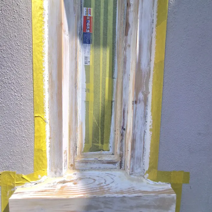 A window frame stripped back to bare wood and masked with yellow tape